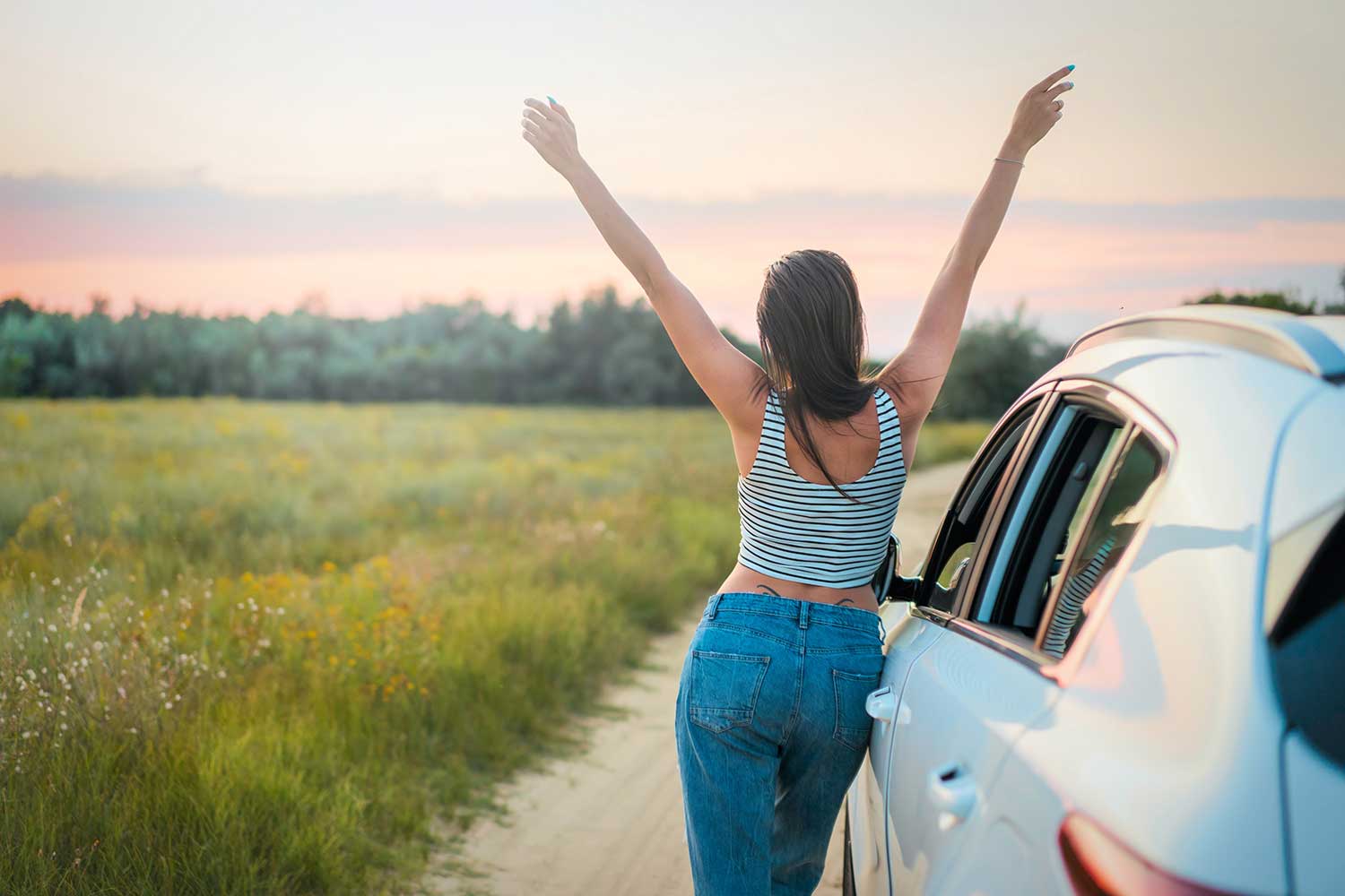 girl with her hands up leaning on a car